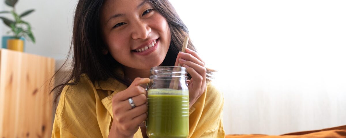 Happy Teen Asian Girl Showing Healthy Green Juice Looking At Cam
