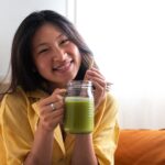 Happy Teen Asian Girl Showing Healthy Green Juice Looking At Cam